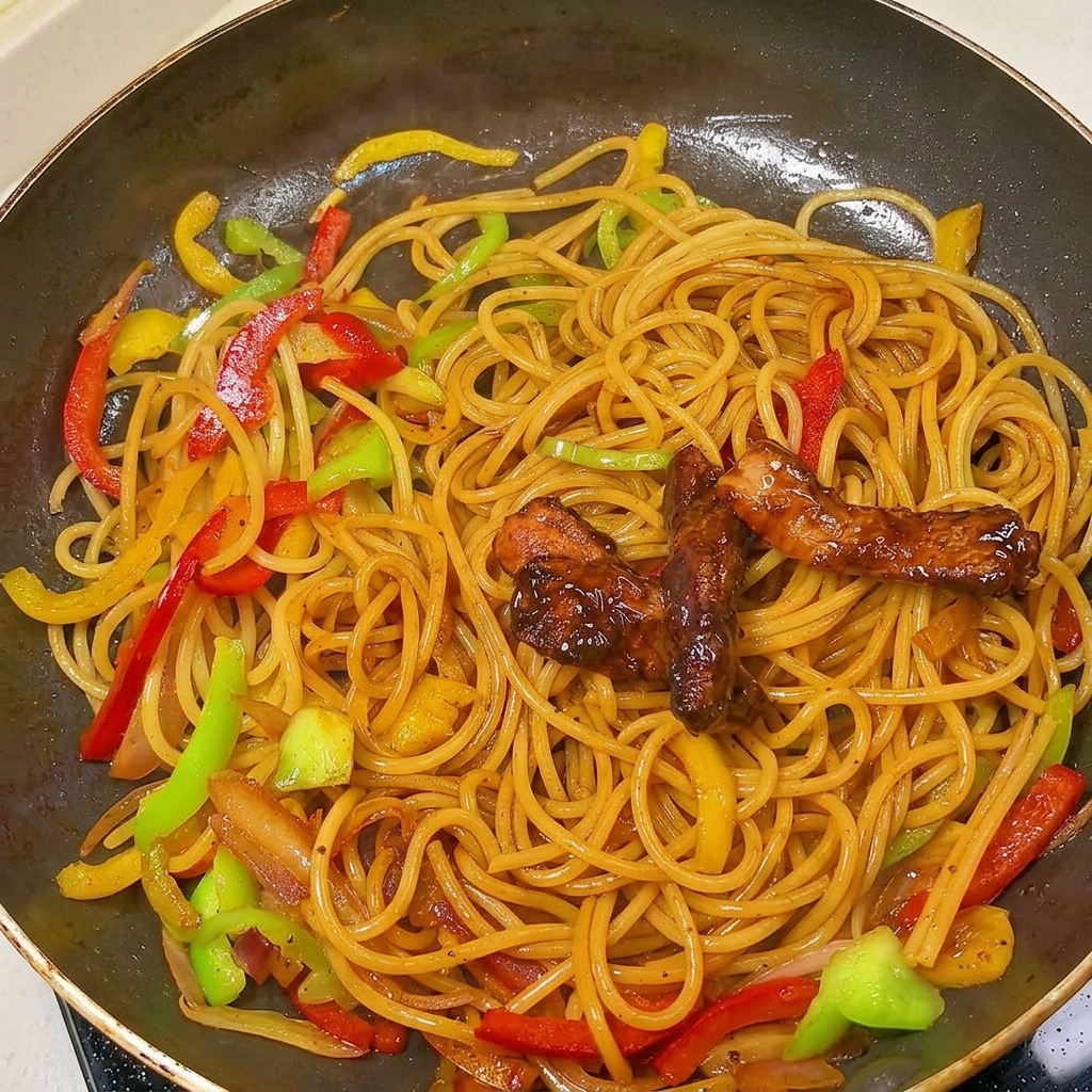 大きなフライパンの中で、黒胡椒パスタとパプリカの上に載せられた炒めた豚肉。