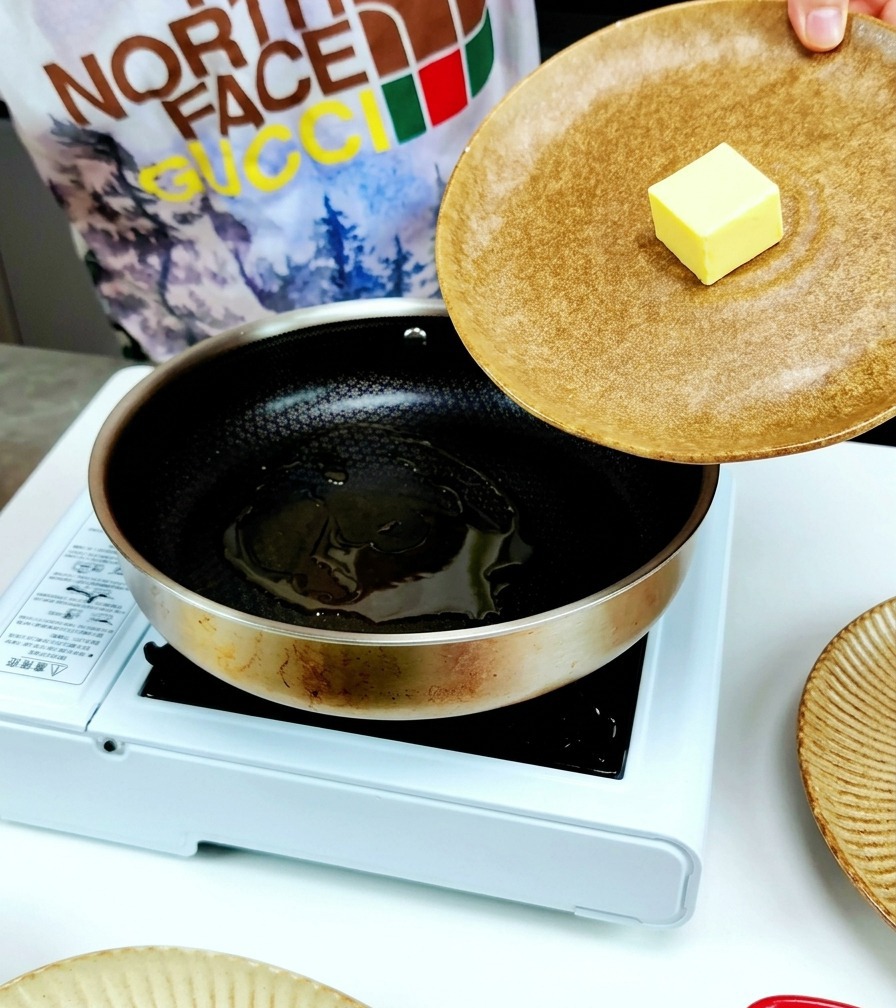 すでにオリーブオイルがひかれているステンレスのフライパンに、黄色いバターの塊を入れている様子