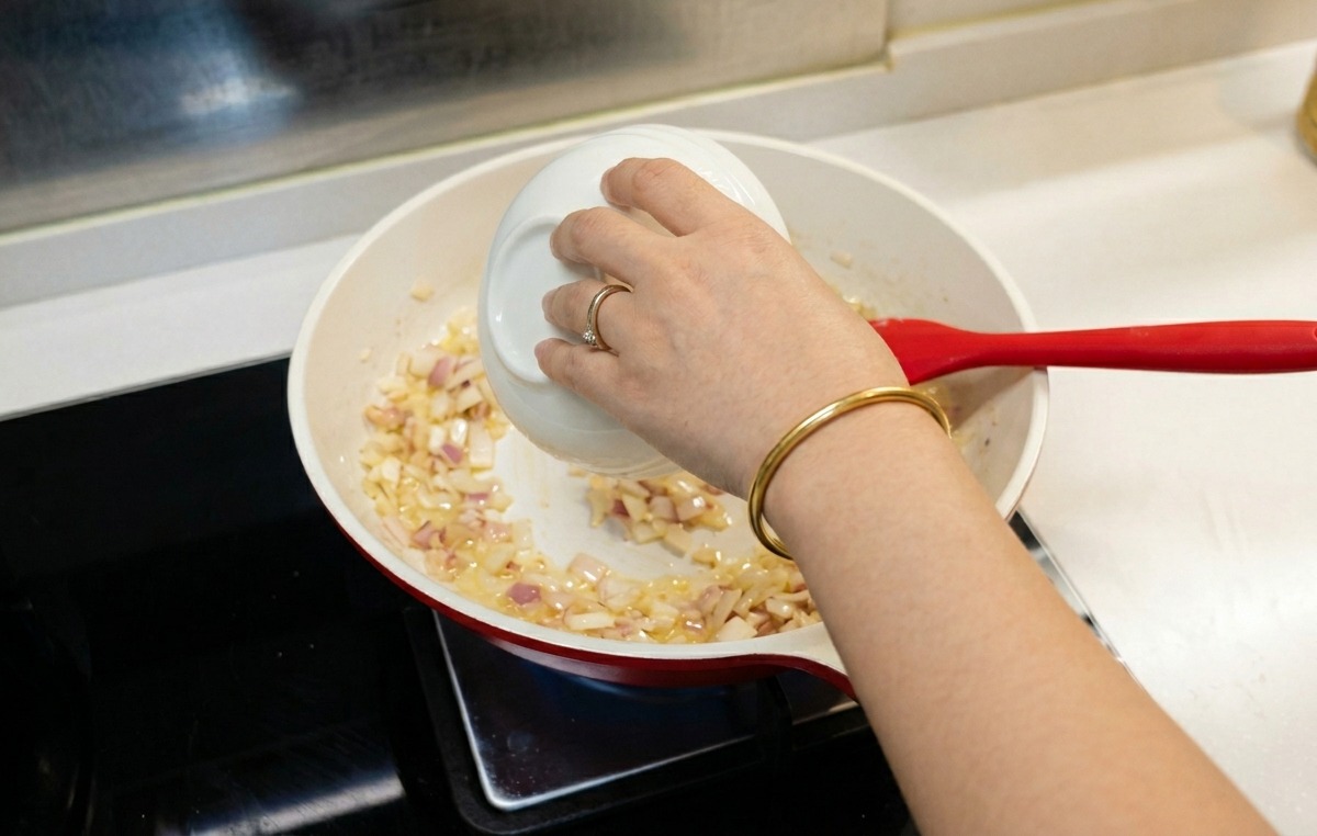 炒めた玉ねぎと薄力粉が入ったフライパンに、小さな白いボウルから水を注いでいる様子。