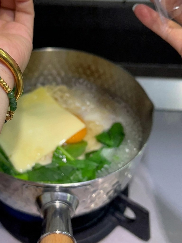 湯気が上がる鍋の中で、卵と麺の上に黄色のスライスチーズをのせている様子