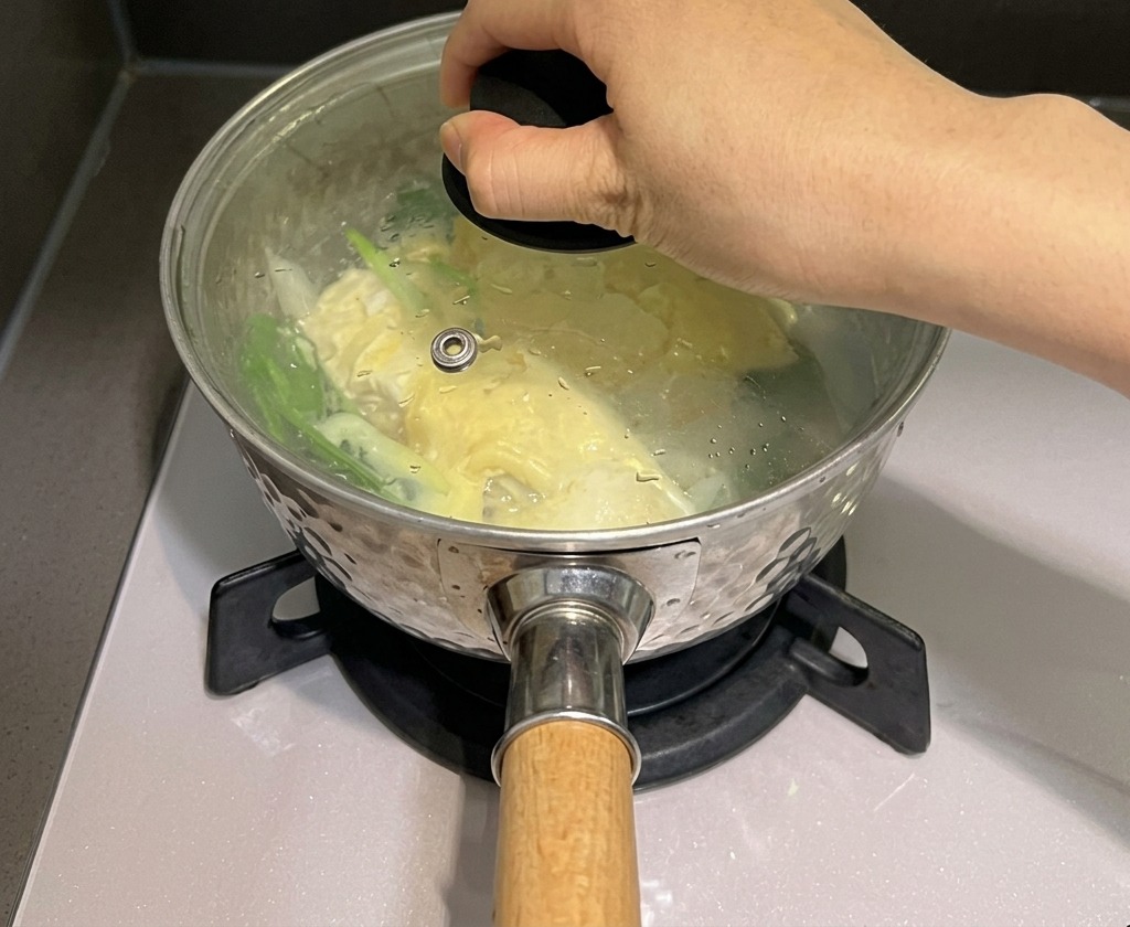 蒸気を閉じ込めるために、麺とチーズが入った鍋に手でガラスのフタをしている様子