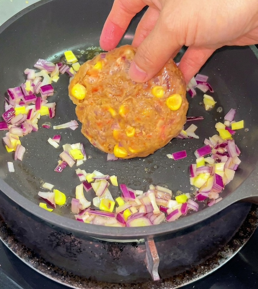 溶けたバターと刻んだ赤玉ねぎが入ったフライパンに、コーンが入った牛ひき肉を入れようとしている様子。