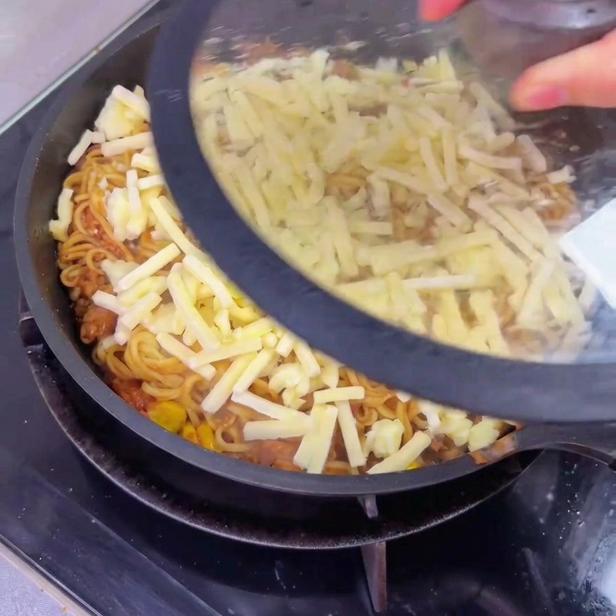 まだ溶けていないチーズがのった牛肉麺のフライパンに、透明なガラスの蓋を被せている様子。