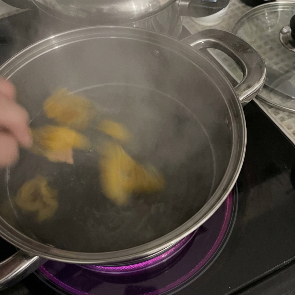 IH調理器の上のステンレス鍋で、沸騰したお湯に黄色いリガトーニを投入する手元の様子。