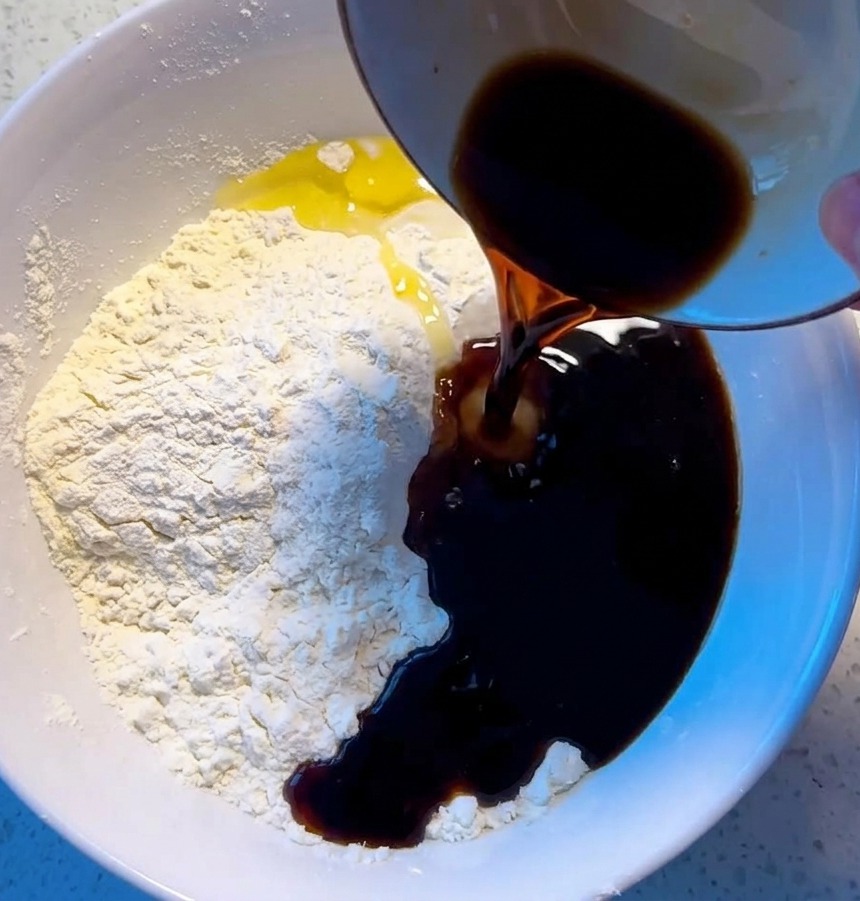 白いボウルに入った小麦粉に液体を注ぎ、木箸で混ぜてまとまりのないピザ生地を作っている様子。