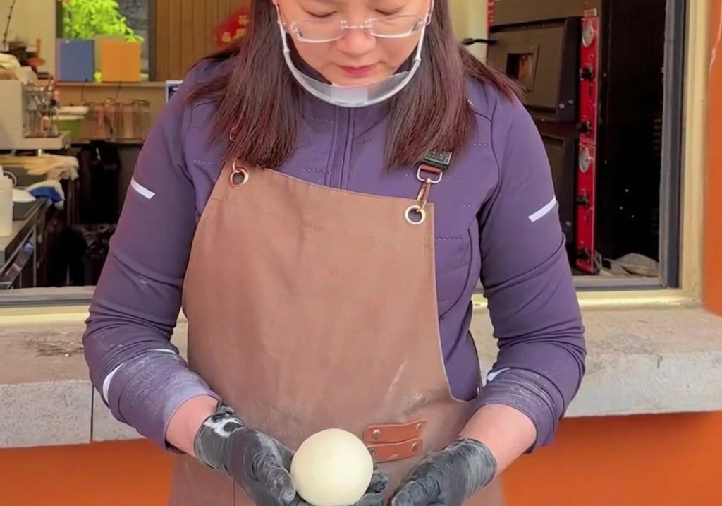 生のピザ生地を両手で優しく包み込み、回転させながら表面にハリを持たせて綺麗な丸型に整えている様子。