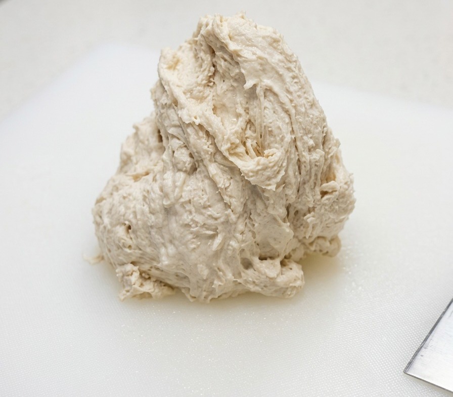 白いプラスチック製のまな板の上に置かれた、水分が多くてベタついたピザ生地の塊。