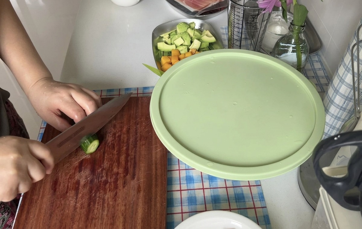 木のまな板の上で、切れ味の良い包丁を使って新鮮なきゅうりを薄い輪切りにしている様子。