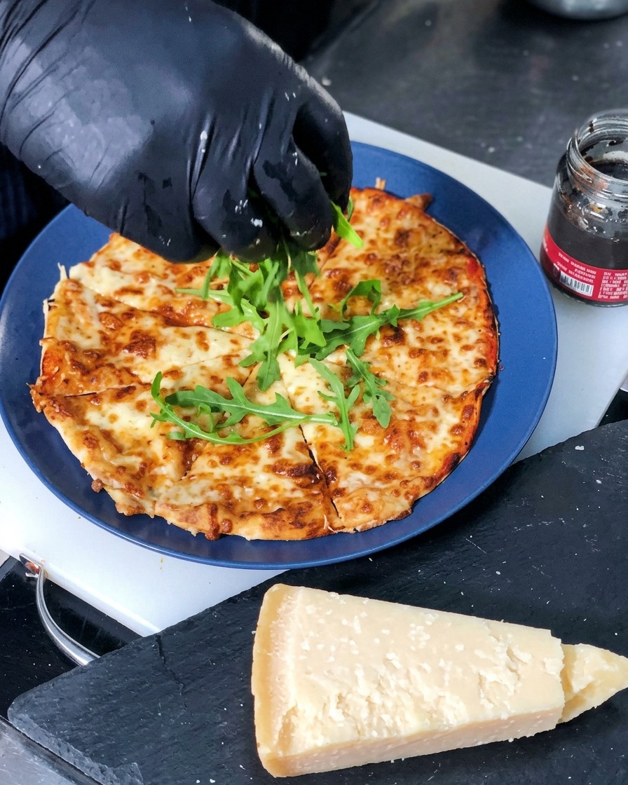 切り分けられた焼き立てのチーズピザの中央に、新鮮な緑のルッコラの葉をのせている様子。