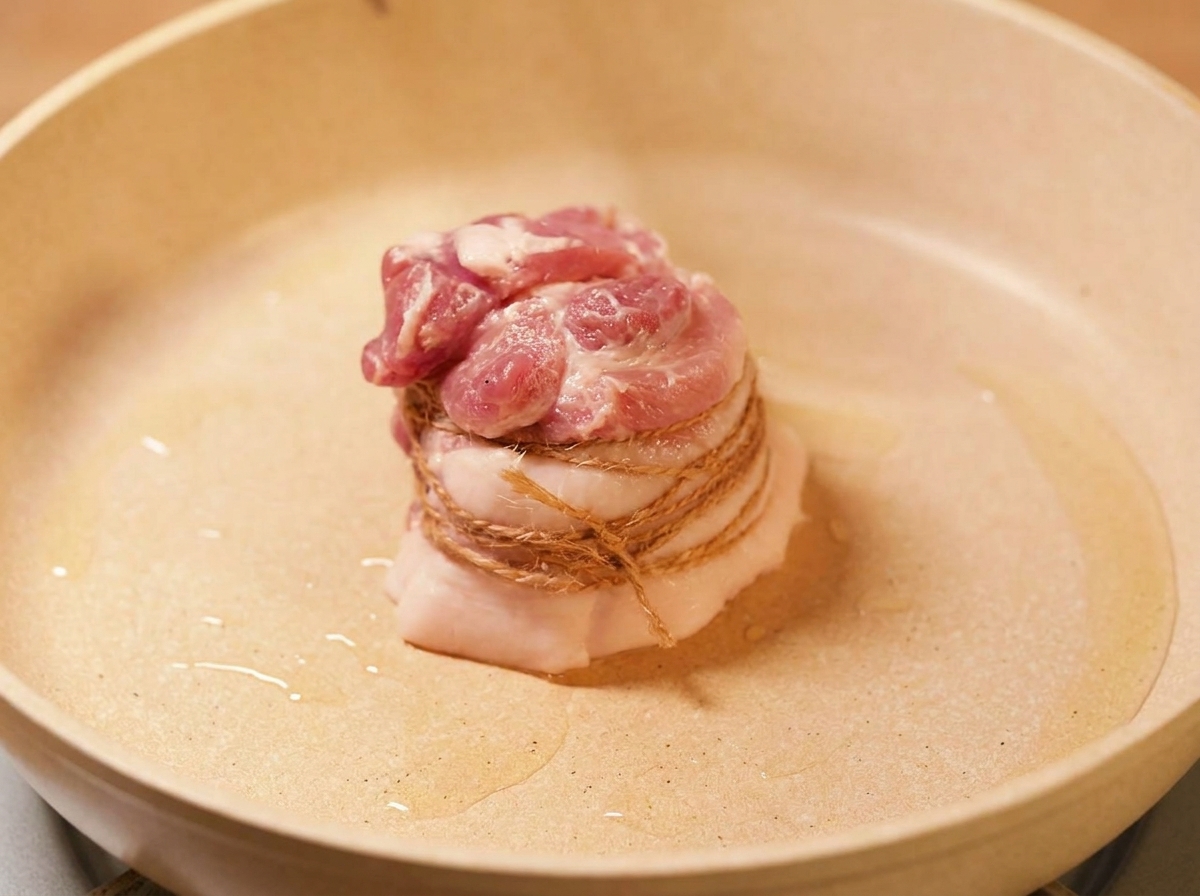タコ糸で縛った豚バラ肉をフライパンで焼き色をつけている様子。