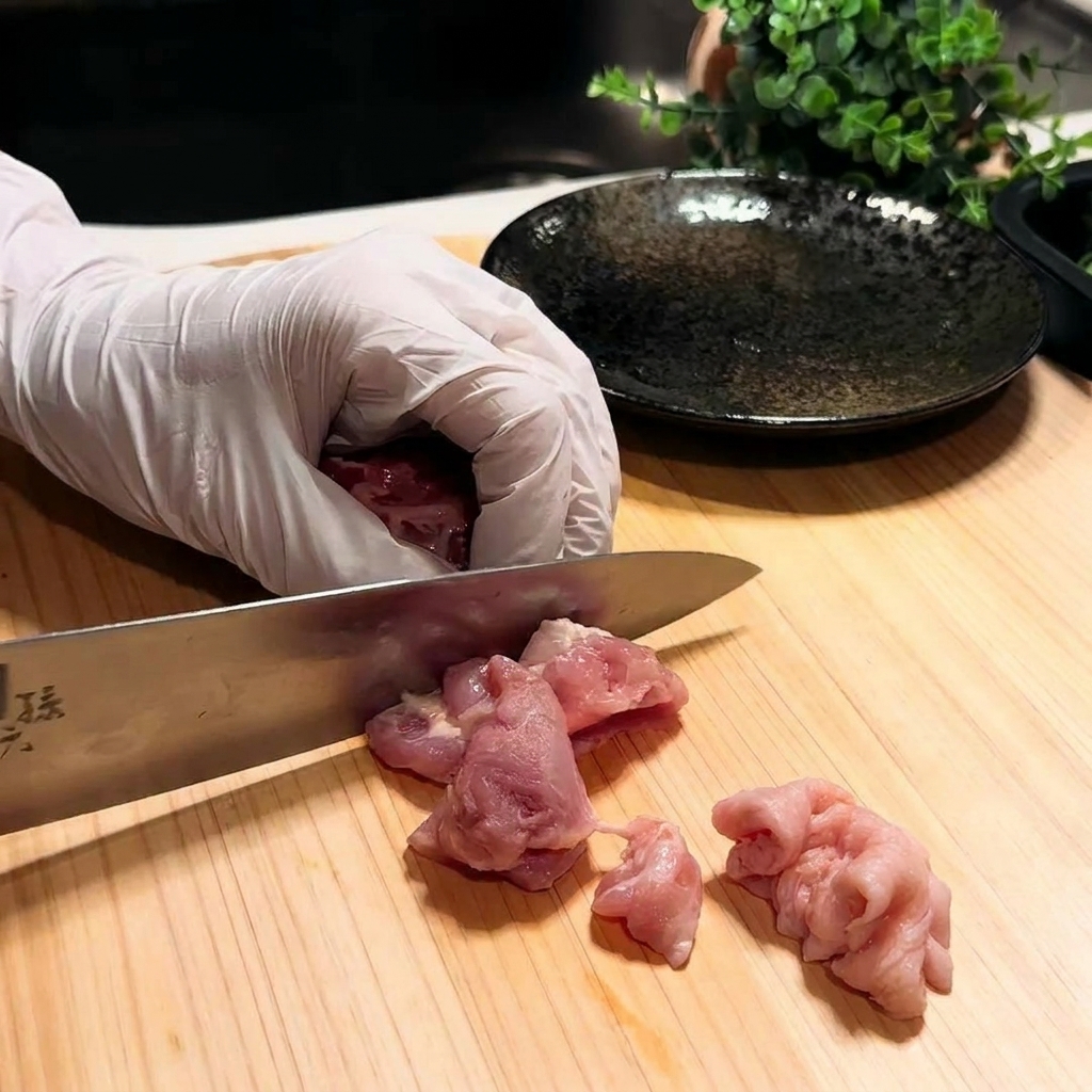 まな板の上で鶏もも肉を一口大に切る様子。