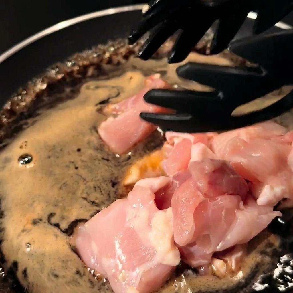 フライパンの煮汁に鶏肉と玉ねぎを加えて煮込む様子。
