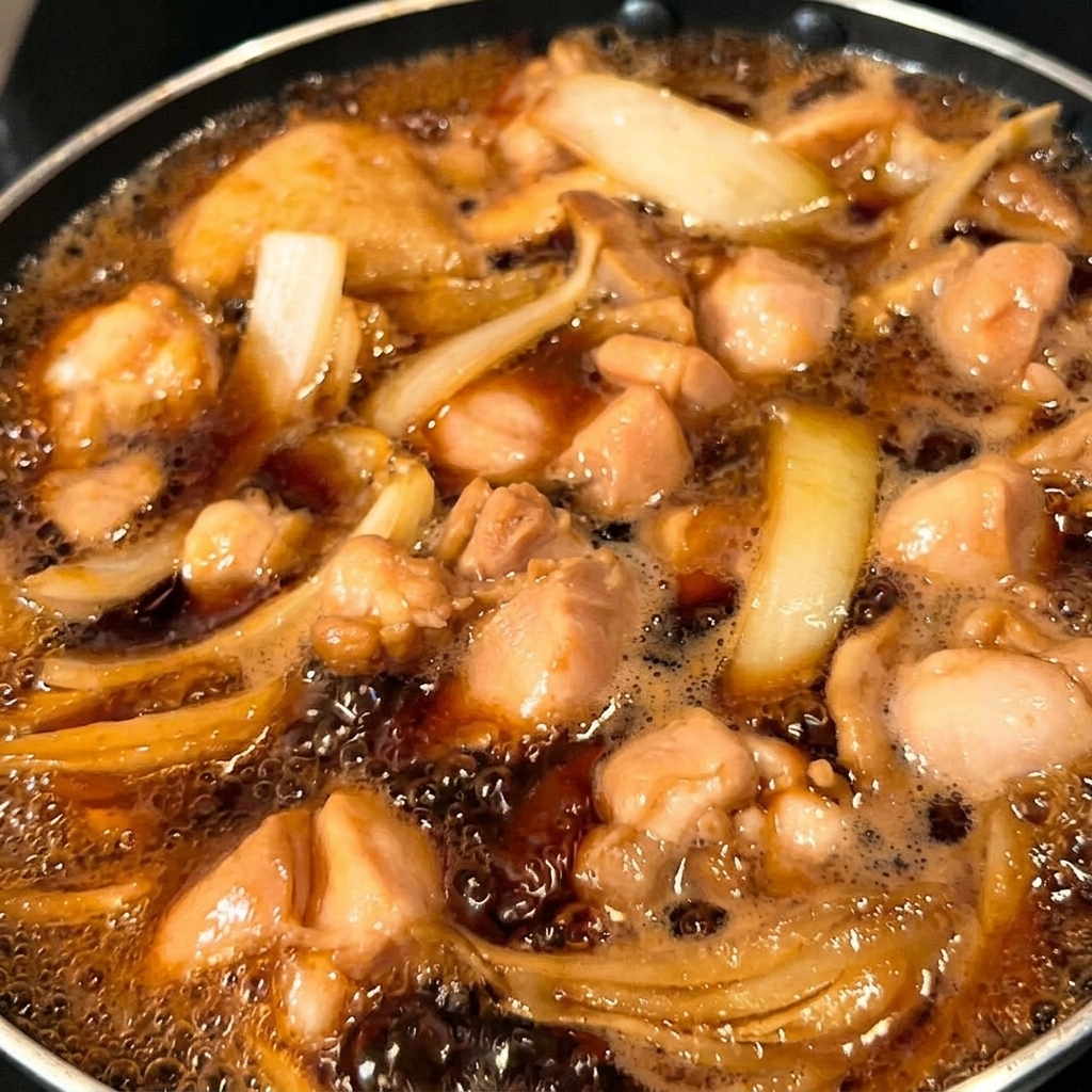 鶏肉と玉ねぎの上に溶き卵の半分を流し入れる様子。