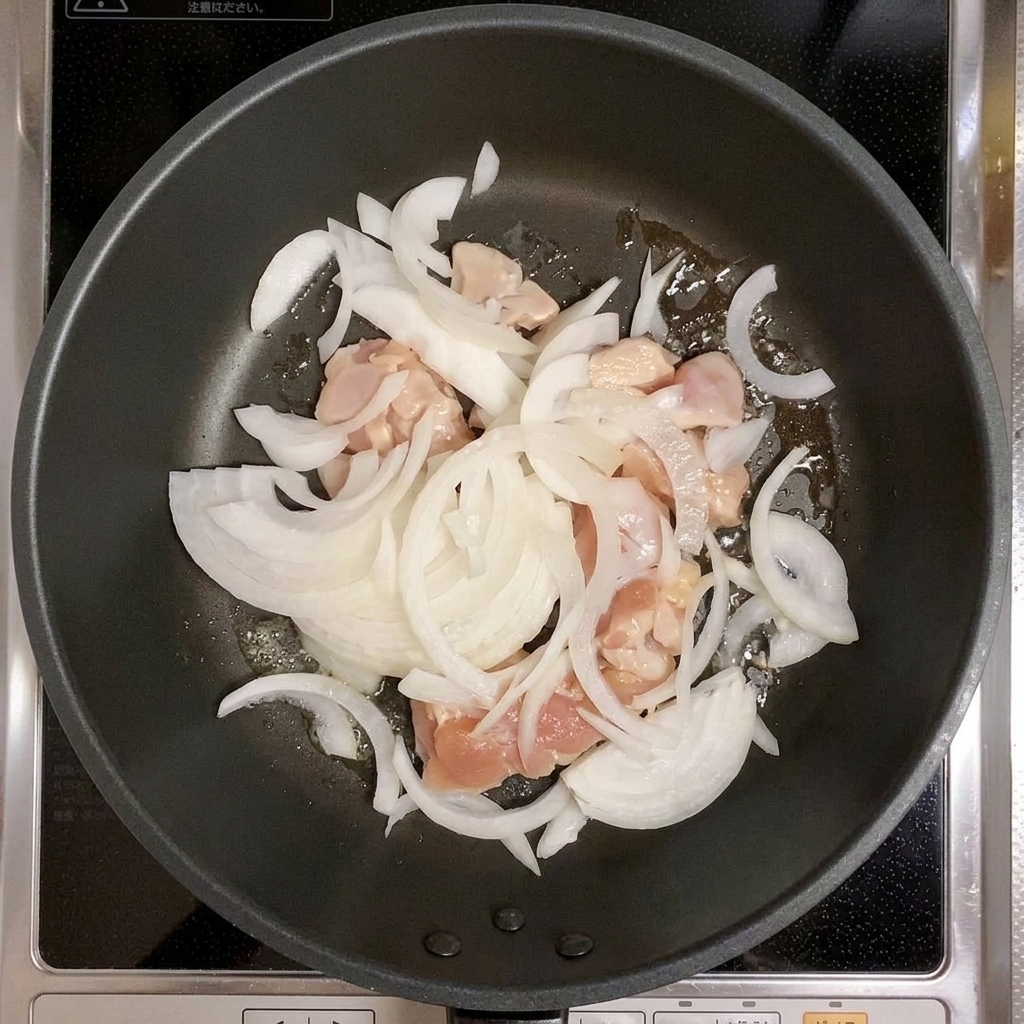 フライパンで鶏肉と玉ねぎを炒めている様子。