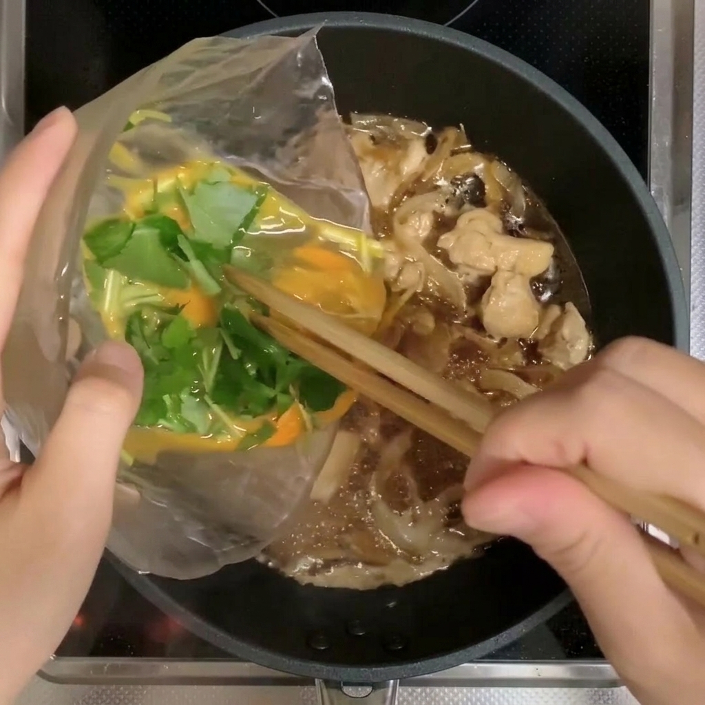 溶き卵と三つ葉をフライパンに回し入れている様子。