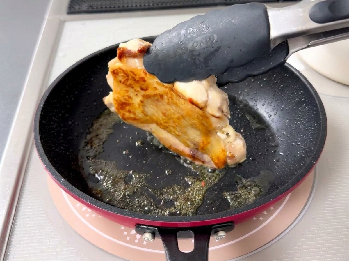 焼き色がついた鶏肉をトングで裏返している様子