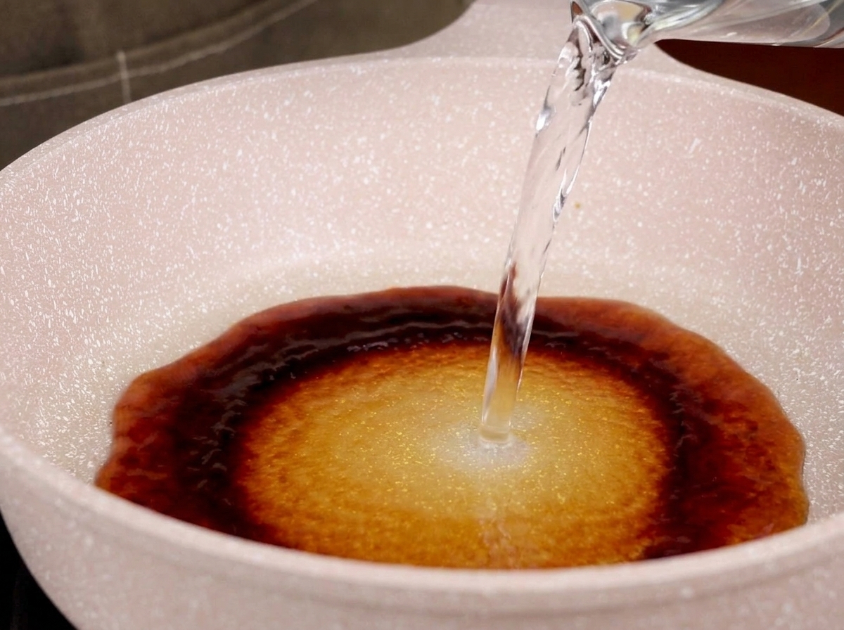 フライパンの照り焼きのたれに水を注ぎ、煮汁を作っている様子。