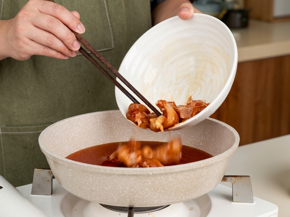 菜箸を使って、照り焼きのたれが入ったフライパンに鶏肉を入れている様子。
