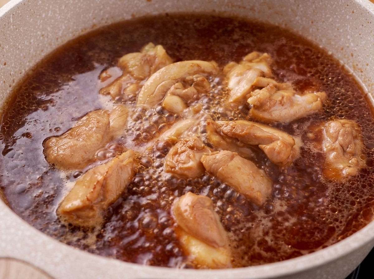 煮立たせた鶏肉と照り焼きのたれの表面から、アクをすくい取っている様子。