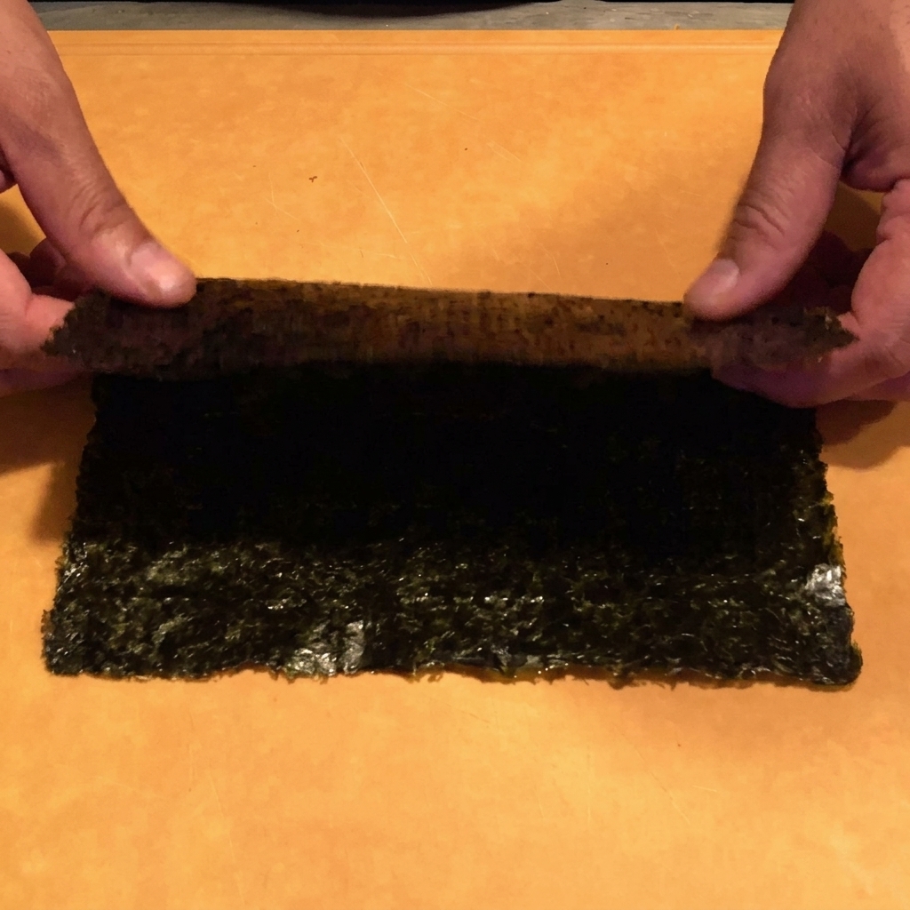 ボウルの上で、キッチンバサミを使って黒い海苔を細い線状に切っている手元のアップ。