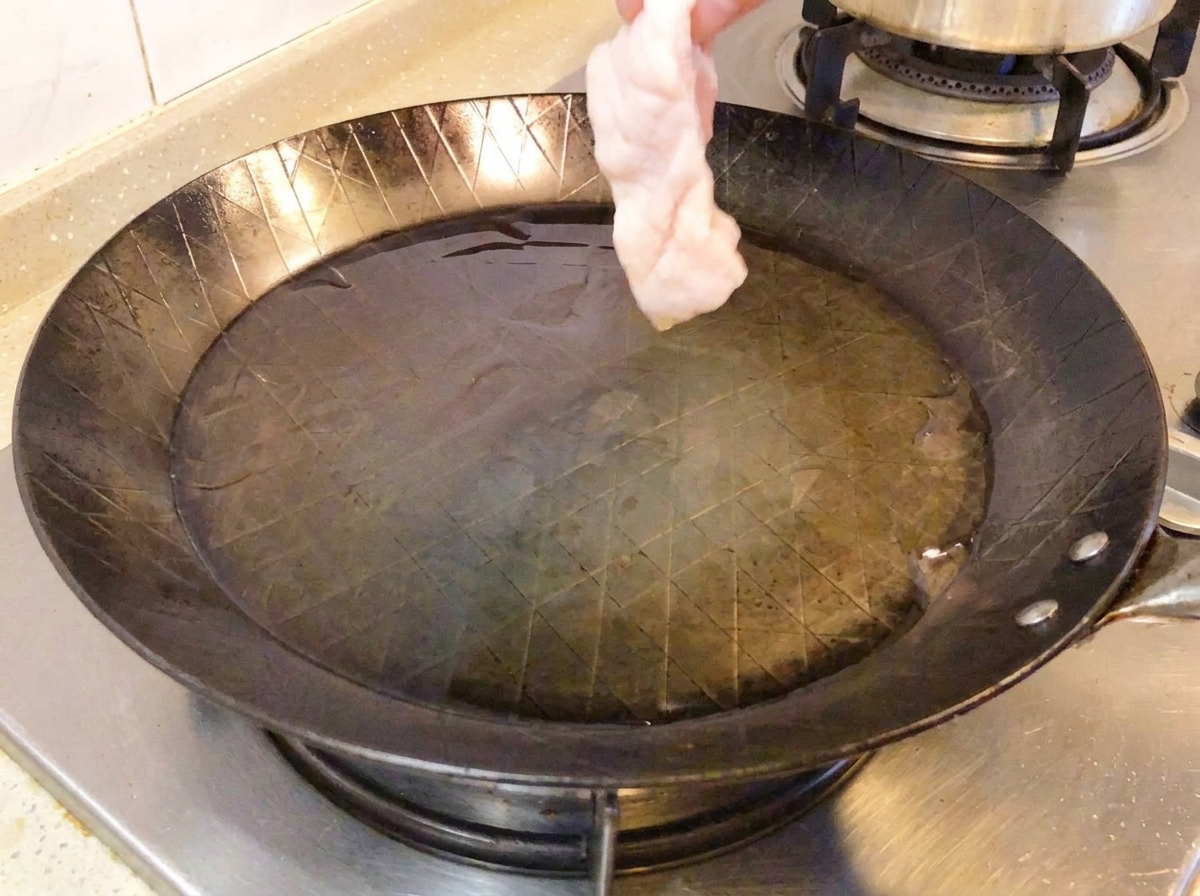 熱したフライパンの中で、生の鶏もも肉が皮目を下にして焼かれている様子。
