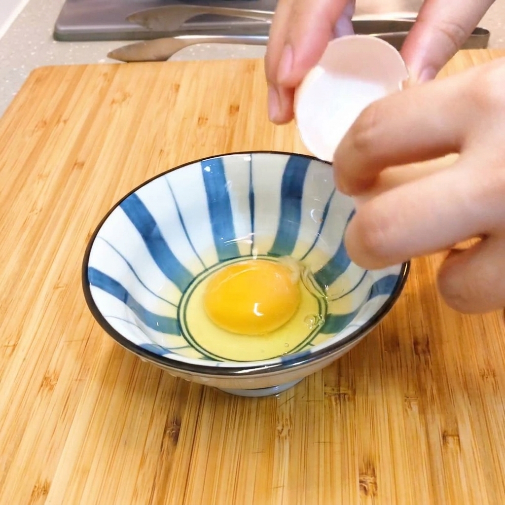 青と白のストライプ模様の陶器のボウルの中で、2個の生卵を箸で軽く混ぜている様子。