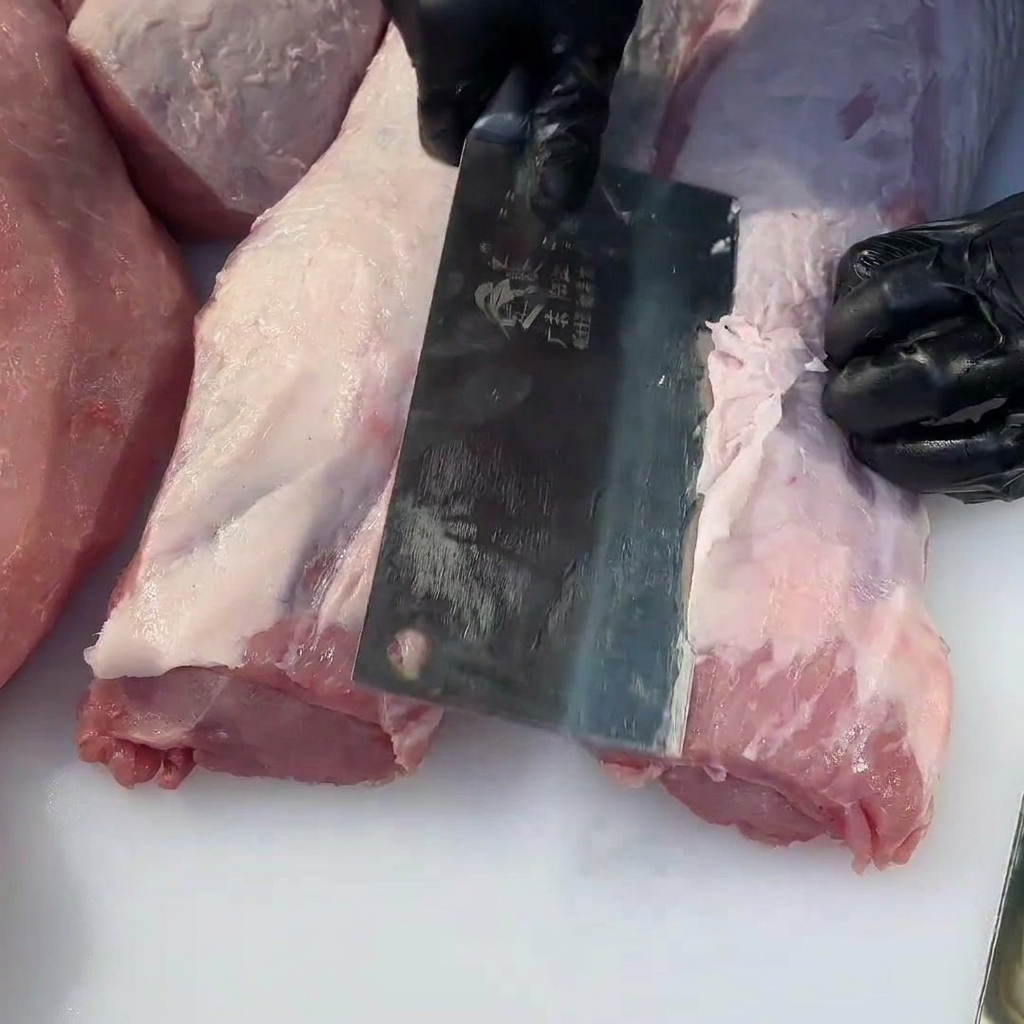 肉切り包丁で豚ヒレ肉の余分な脂を取り除いている様子。