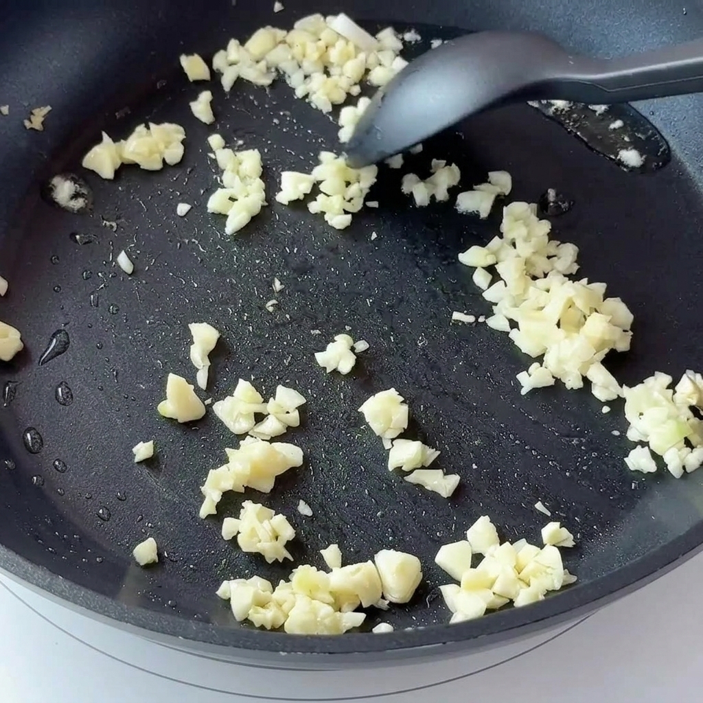 黒い焦げ付き防止フライパンでみじん切りのにんにくと角切りの玉ねぎを炒めている様子。