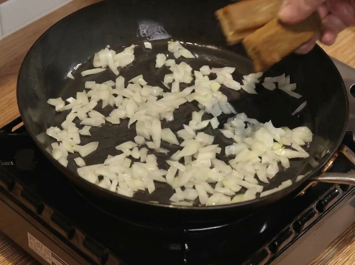 フライパンで炒めた玉ねぎにカレールーと水を加えて混ぜている様子。