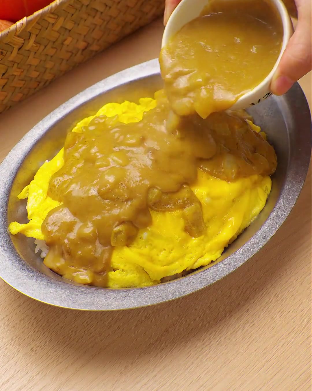 小さなボウルから、スクランブルエッグとご飯の上に濃厚な黄色いカレーソースをかけている様子。