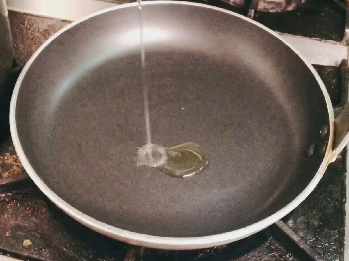 コンロに置かれた黒いフライパンにサラダ油を注いでいる様子。