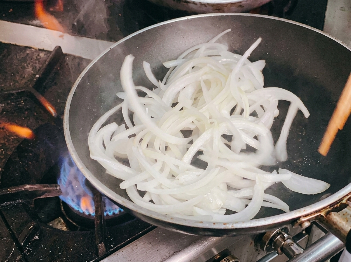 フライパンに入れた玉ねぎを菜箸で炒めている様子。