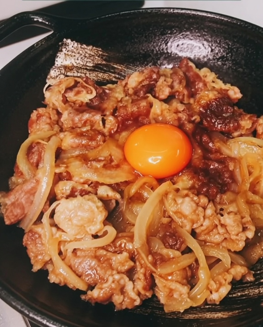 牛丼の中央に、鮮やかなオレンジ色の卵黄をのせた様子。