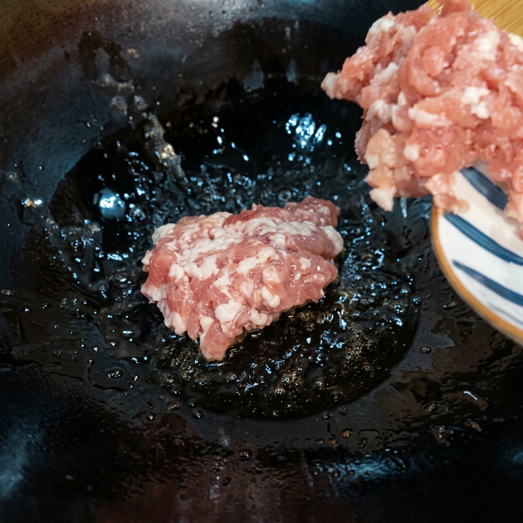 熱したフライパンで挽肉を中弱火で焼き色がつくまで炒めている様子。