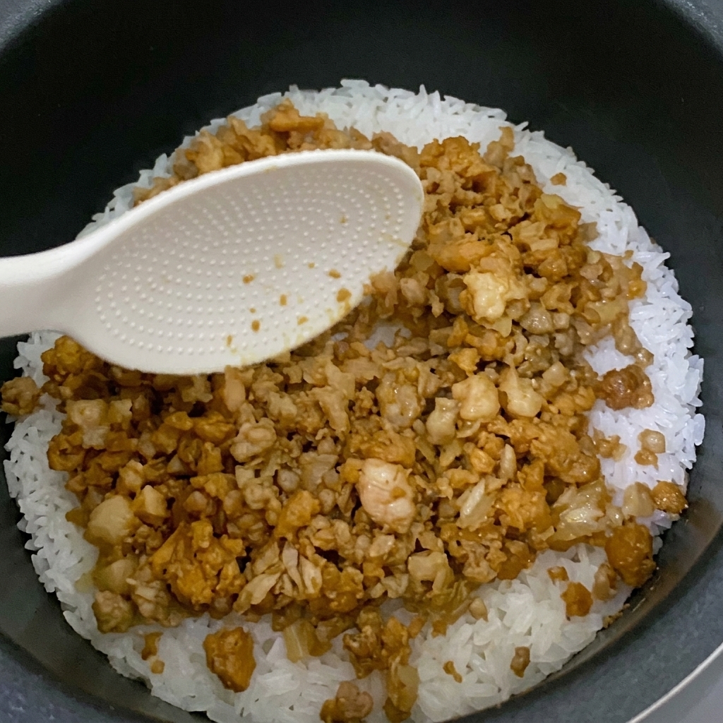 炊飯器のご飯の上に炒めた具材を乗せている様子。