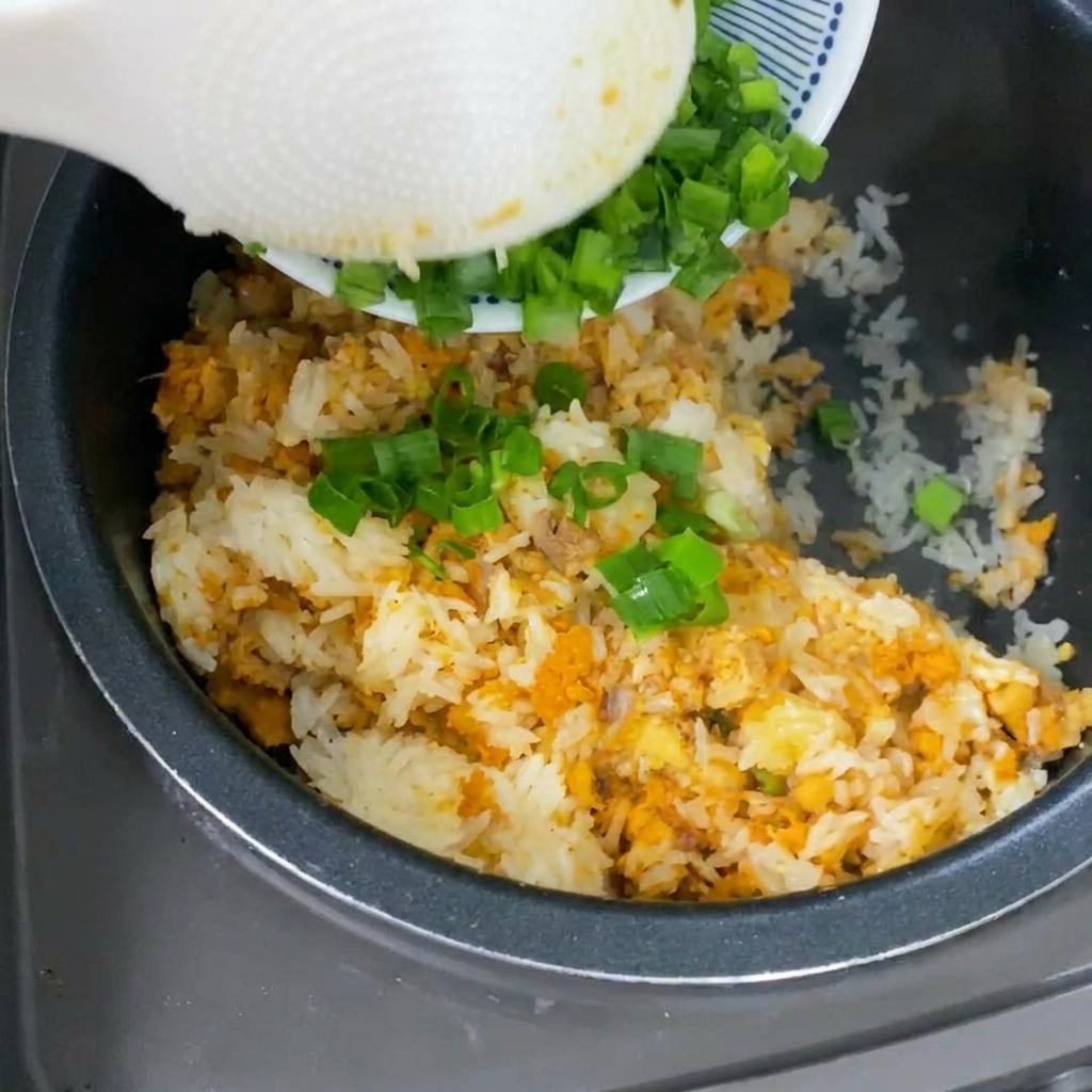 炊き上がった黄色いご飯に新鮮な刻みネギをのせている様子。