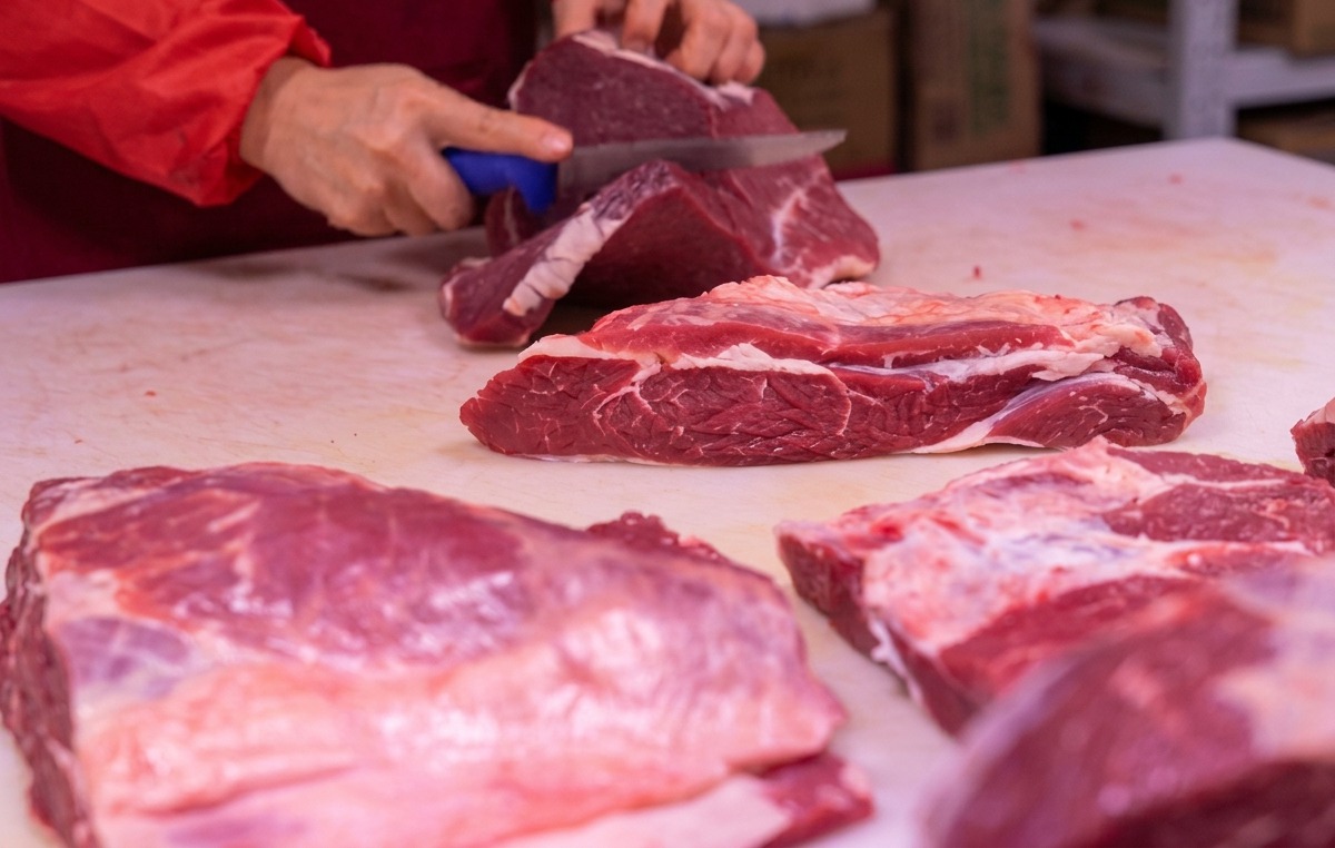 白いまな板の上で、鋭い包丁を使って赤身肉をカットする手。