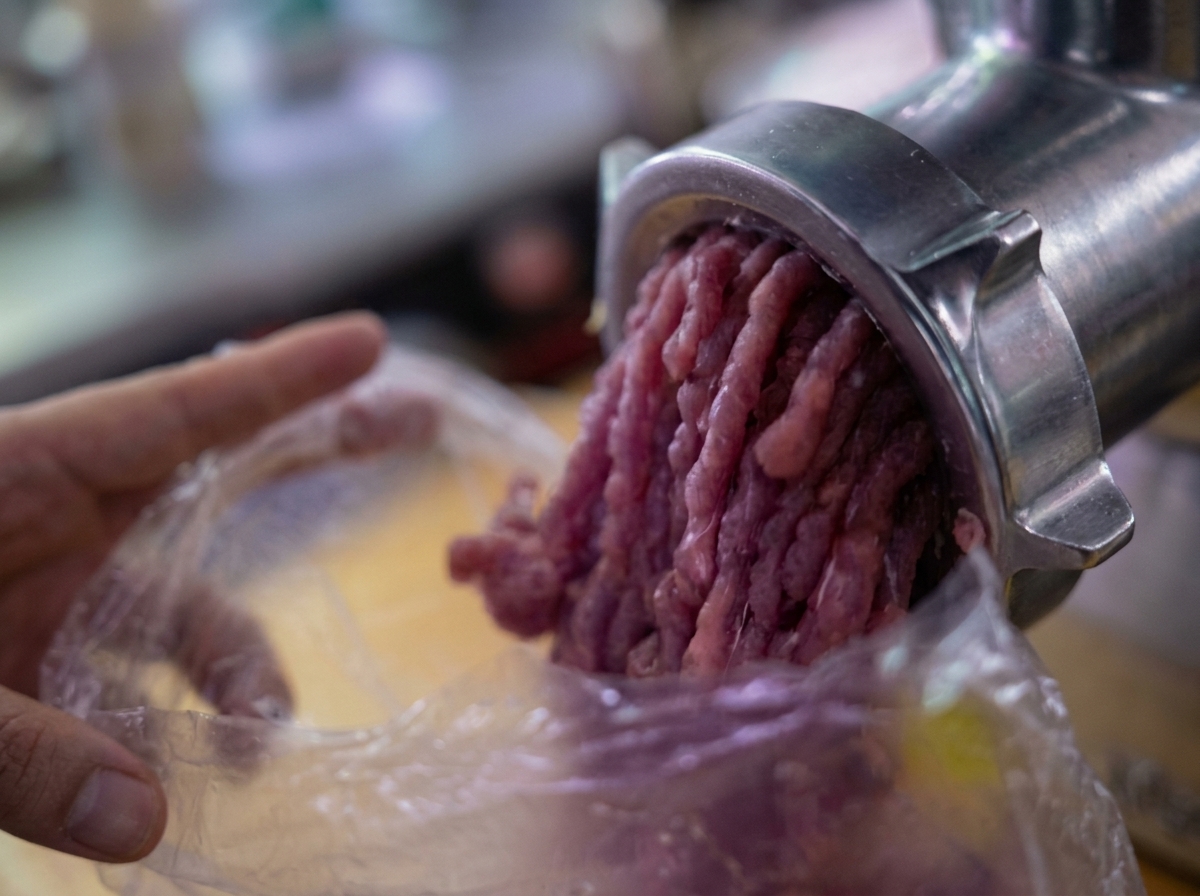 機械式の肉挽き機からビニール袋の中に挽肉が出てきている様子。