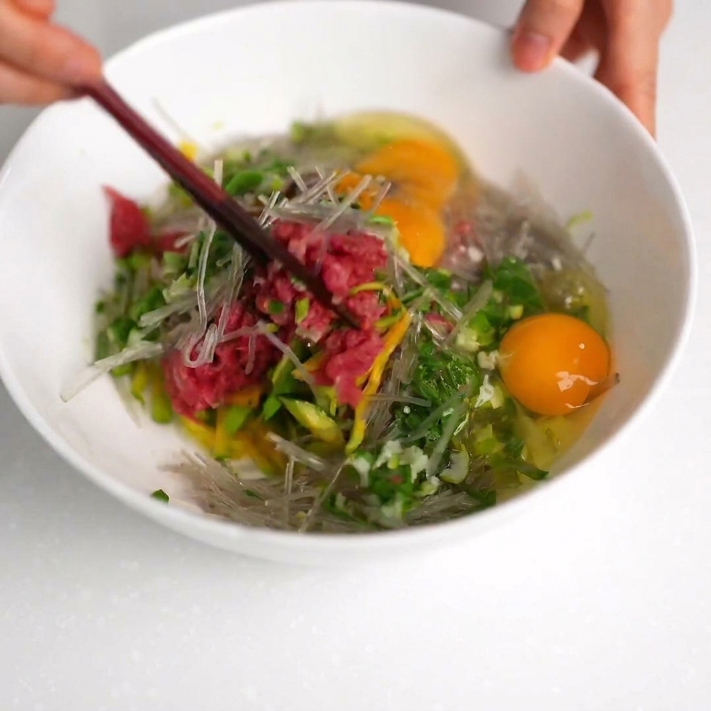 白いボウルの中で、お箸を使って牛肉と野菜の生地をかき混ぜている様子。