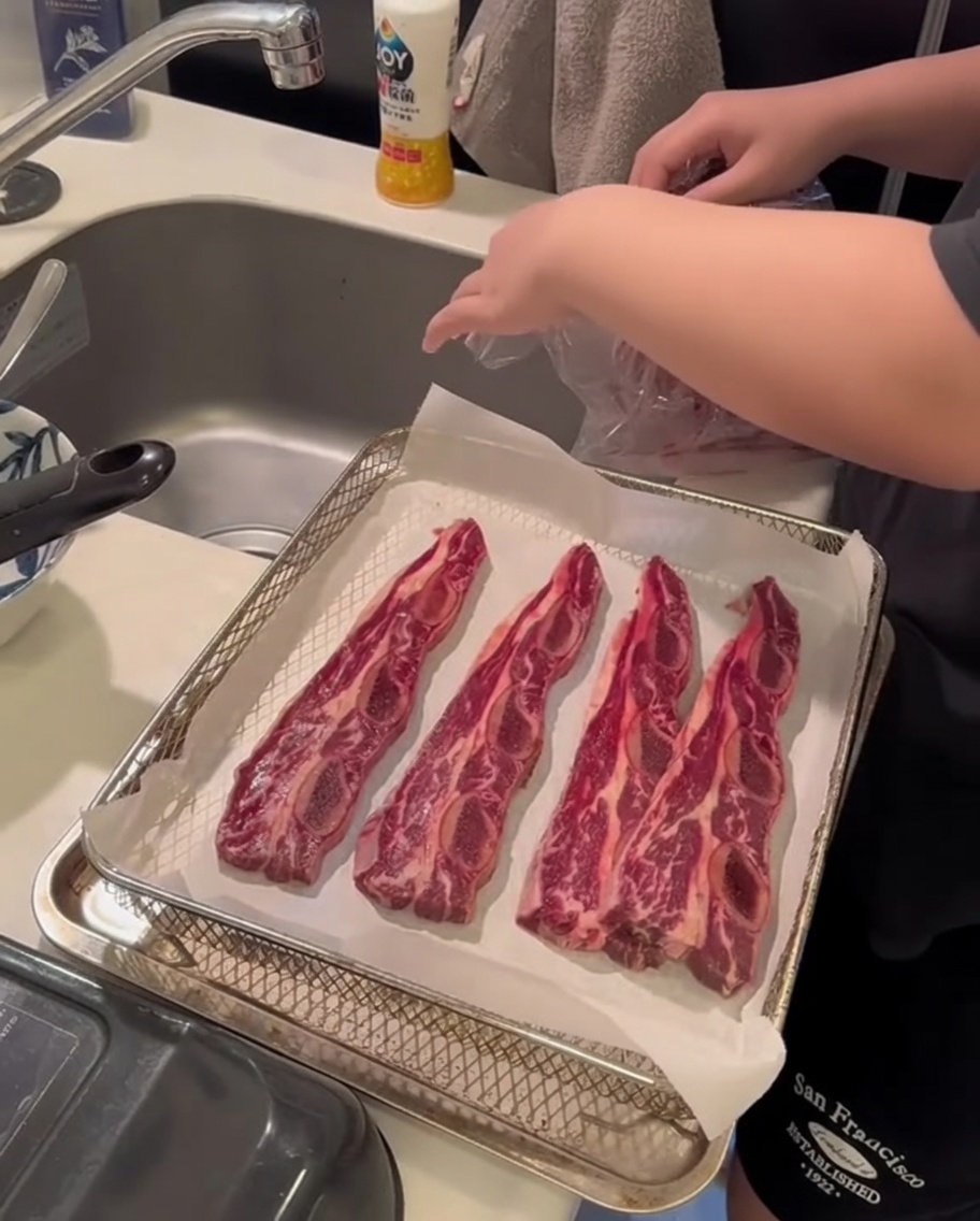 ペーパータオルを使って骨付きカルビの表面の水分を押さえる手元のアップ。