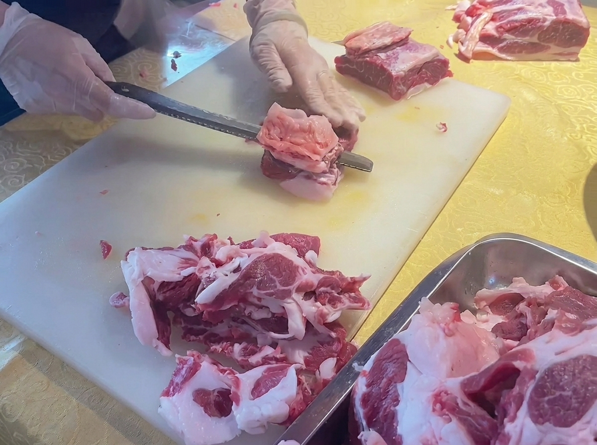 まな板の上で、新鮮な牛カルビ肉から余分な脂を包丁で取り除いている様子。