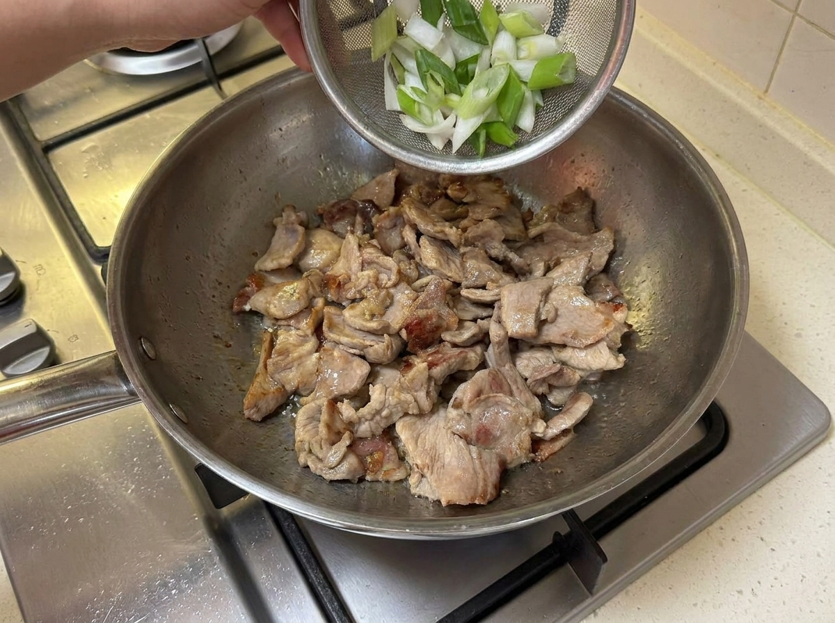 焼き色のついた豚肉が入ったフライパンに、切った長ねぎを加えているところ。