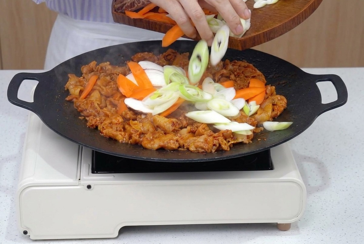 炒めた豚肉に、切った野菜類を加えて一緒に炒めている様子。