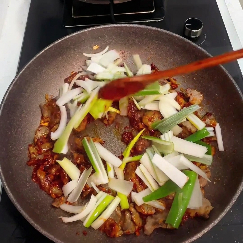 豚肉とタレに刻んだ玉ねぎと青ネギが加えられている様子。