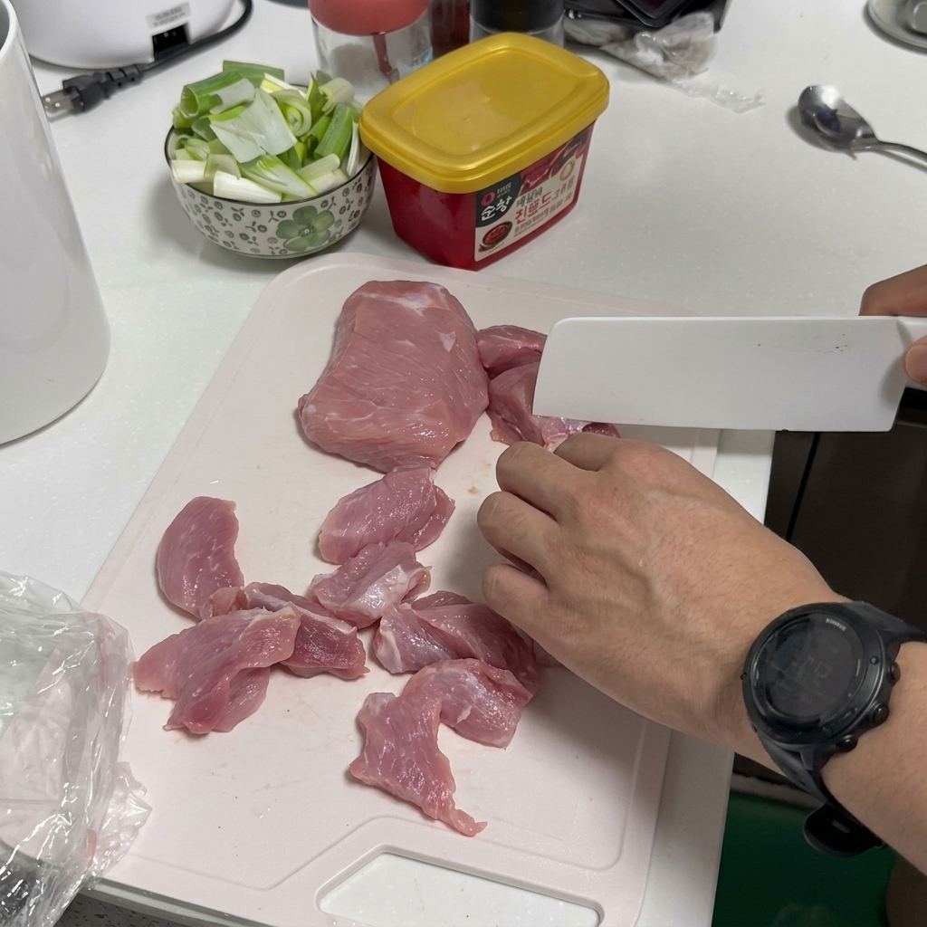 まな板の上で豚肉を包丁で薄く一口サイズに切っている様子。