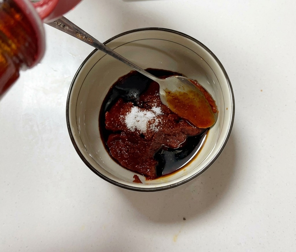 小さなボウルにコチュジャン、調味料を入れ、スプーンで混ぜている様子。