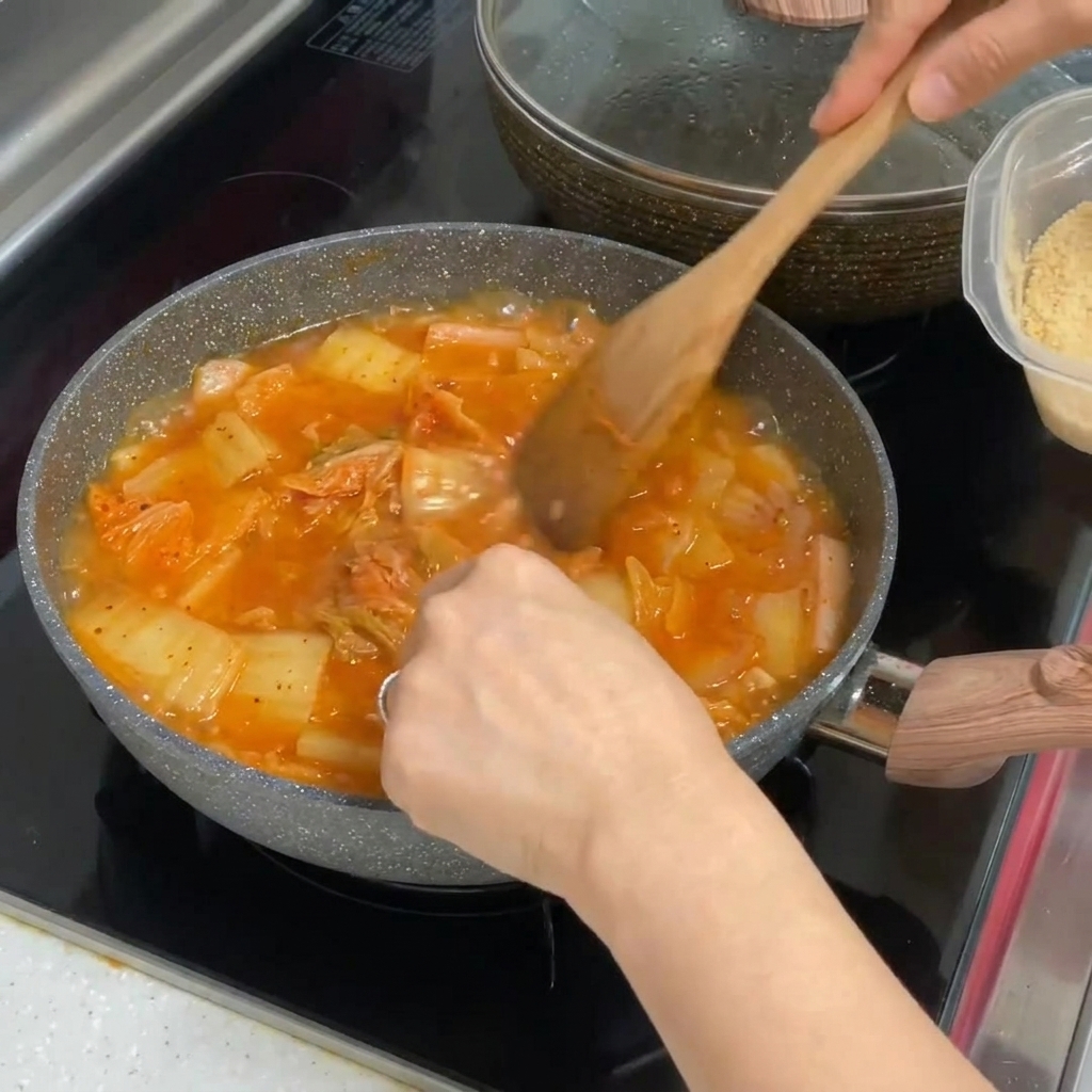 グツグツ煮立つ真っ赤なキムチチゲの鍋に、おろしにんにくを混ぜ込んでいる様子。