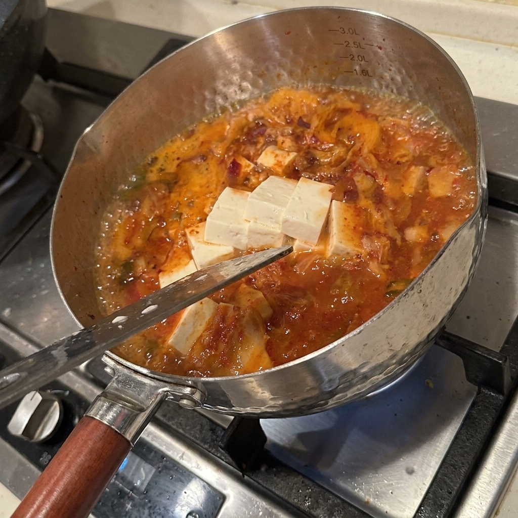 赤くスパイシーなスープの中で、豆腐、えのき茸、キムチがグツグツと煮込まれている様子。