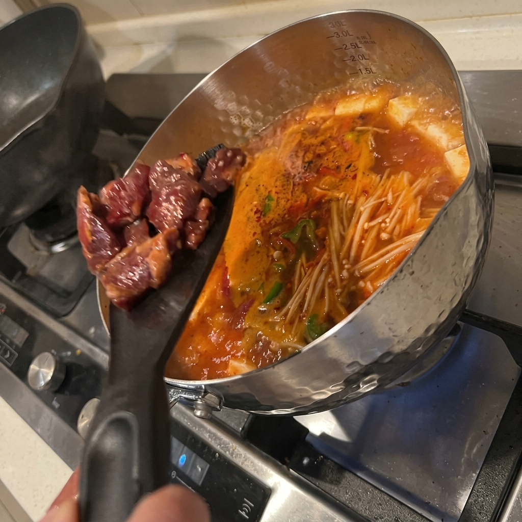 キムチと豆腐のスープが煮え立つ鍋に、マリネしておいた牛肉を加えている様子。