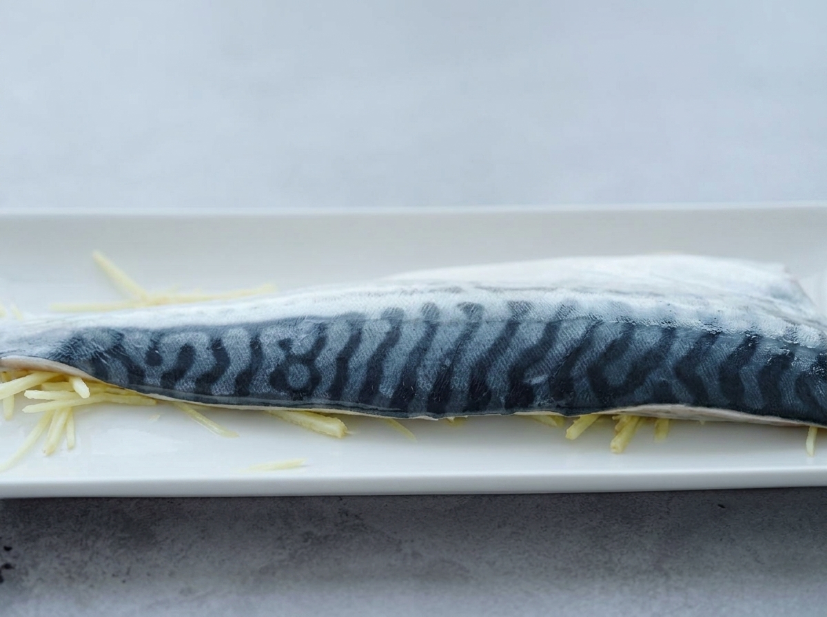 千切り生姜を敷いた上に鯖を置き、料理酒をかけている様子。